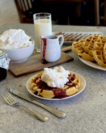 Buttermilk waffles with berry sauce and whipped cream. Glass of milk, plate of waffles, and jar of berry sauce.