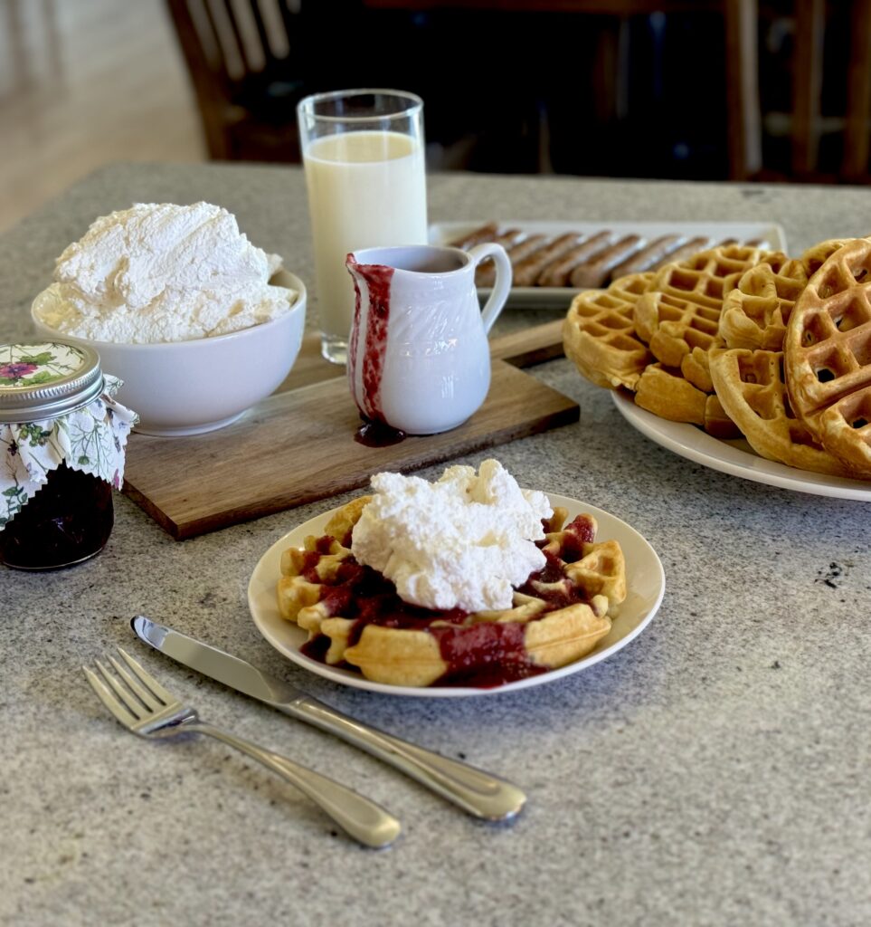 Buttermilk waffles with berry sauce and whipped cream. Glass of milk, plate of waffles, and jar of berry sauce.