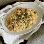 Creamy noodles with shrimp and herbs on plate.