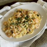 Creamy noodles with shrimp and herbs on plate.