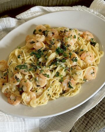 Creamy noodles with shrimp and herbs on plate.