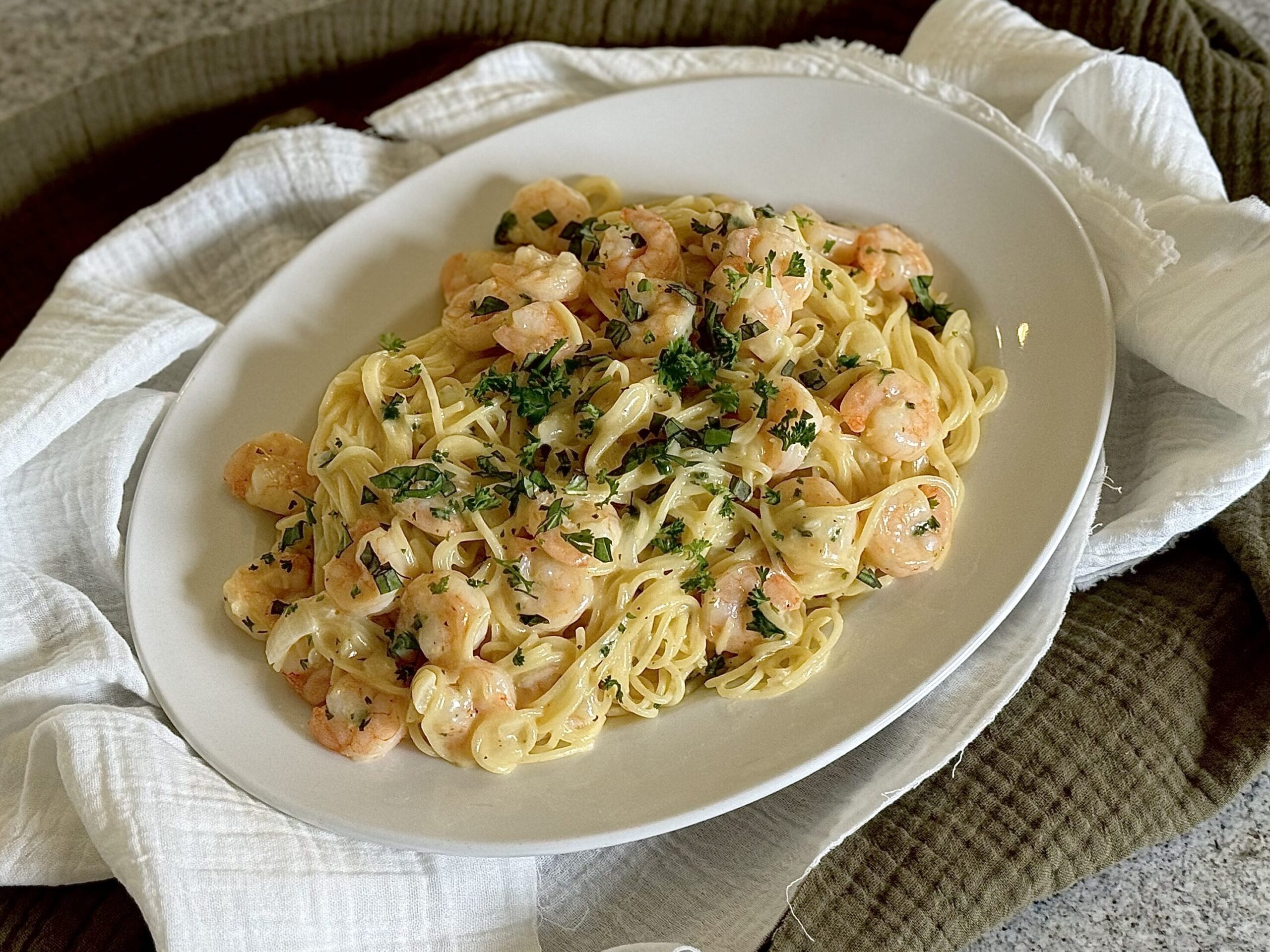 Creamy noodles with shrimp and herbs on plate.